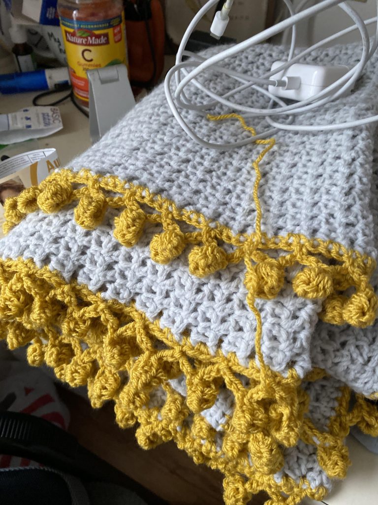 megan's crocheted blanket. gray body with mustard yellow pom pom border